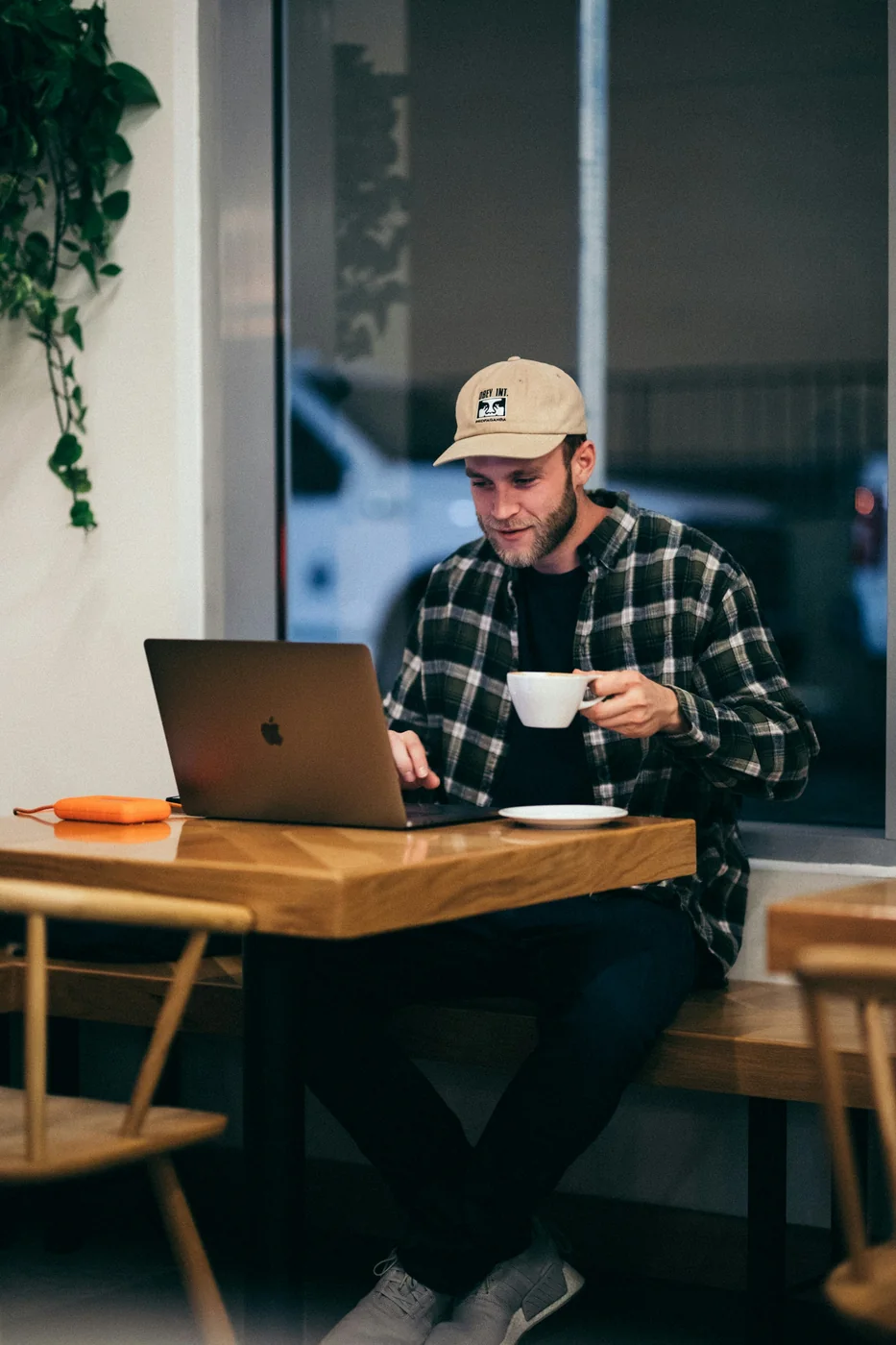 A man with a coffee working on his laptop by a window